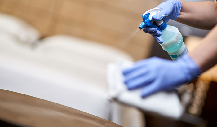 A person wearing blue gloves cleaning a bed with a cloth, ensuring cleanliness and hygiene.