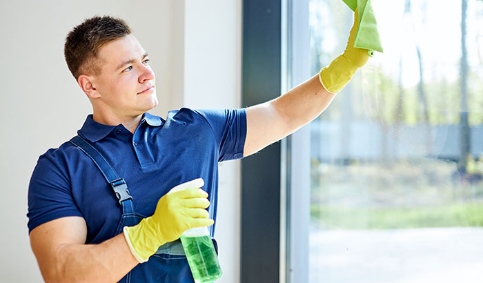 A man wearing a blue shirt and yellow gloves cleaning a window.