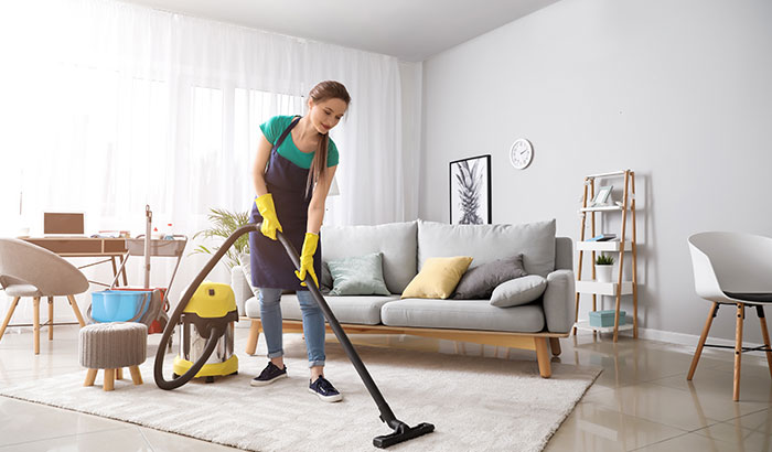 A woman using a vacuum cleaner to clean a living room, focusing on removing carpet stains.