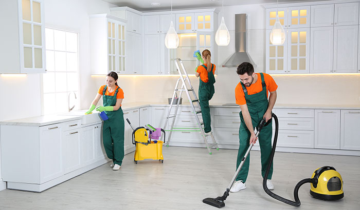 A man and a women cleaning a kitchen together with a vacuum cleaner.