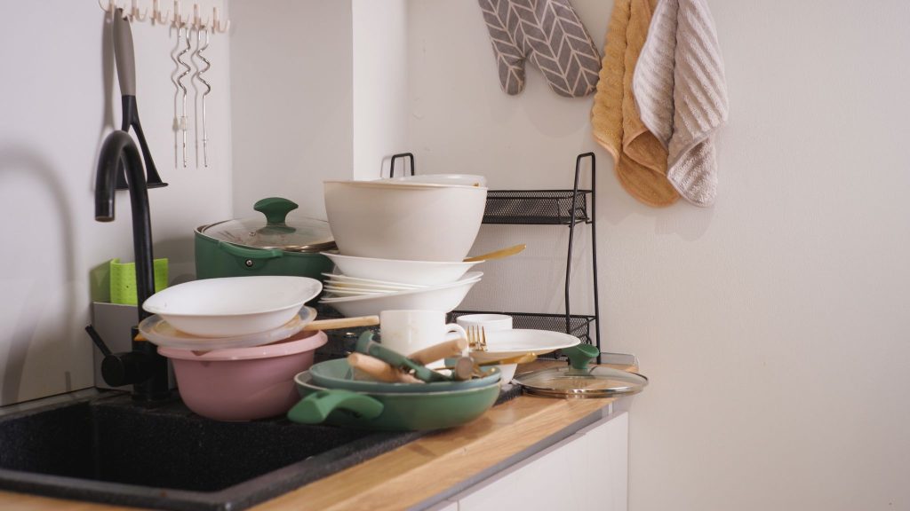A high stack of dirty dishes, bowls, and cookware piled up next to a kitchen sink.
