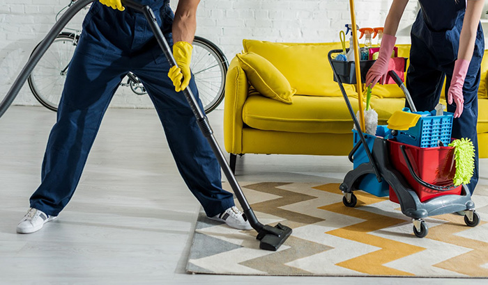 Two People Engaged In Cleaning A Room That Includes A Yellow Couch