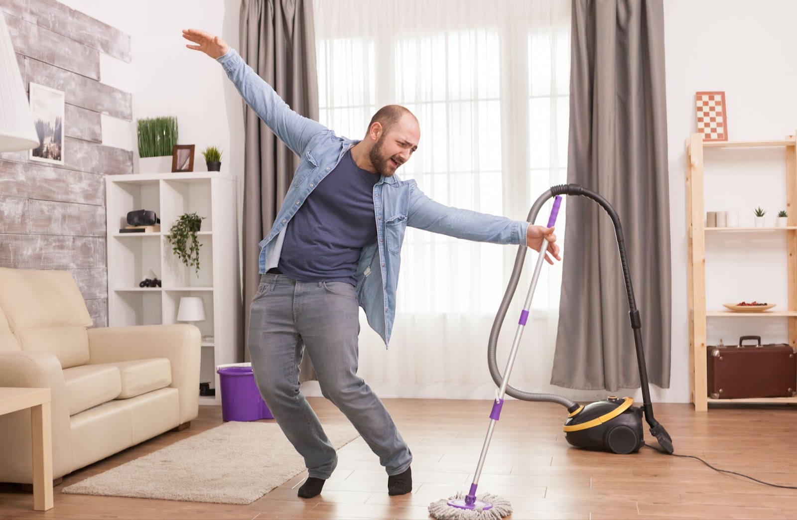A man joyfully dances with a vacuum cleaner in a room. Pre-Cleaning Tips, Cleaning, Declutter