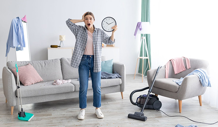 A woman cleans her living room while holding a clock. Pre-Cleaning Tips, Cleaning, Declutter