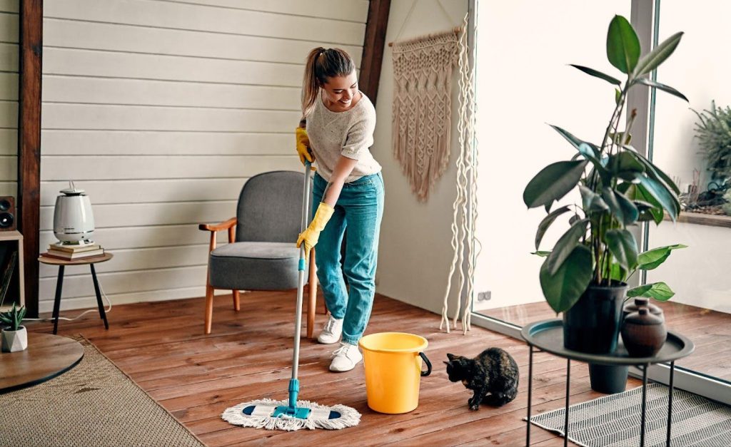 A woman uses a mop to clean the floor in a room, demonstrating effective cleaning techniques
