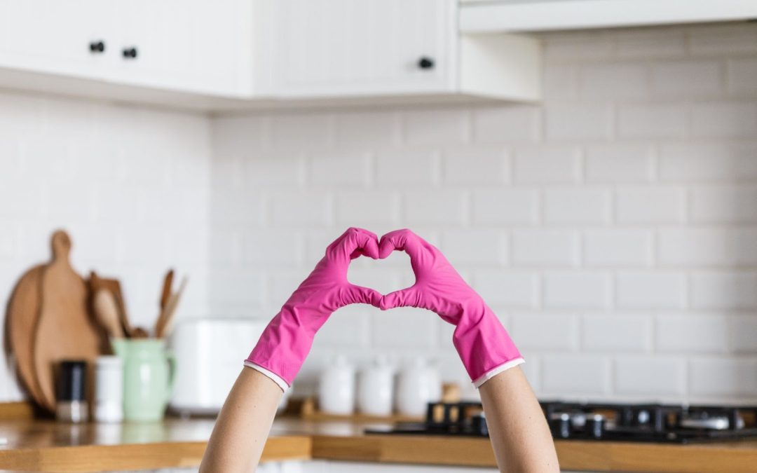 A person wearing pink gloves forms a heart shape with their hands in a modern kitchen.