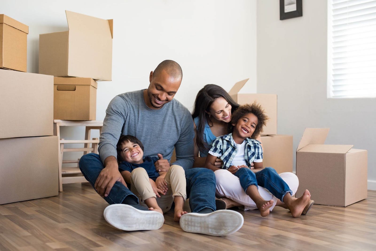 Happy family sitting on the floor, surrounded by moving boxes, smiling and enjoying time together in their new home.