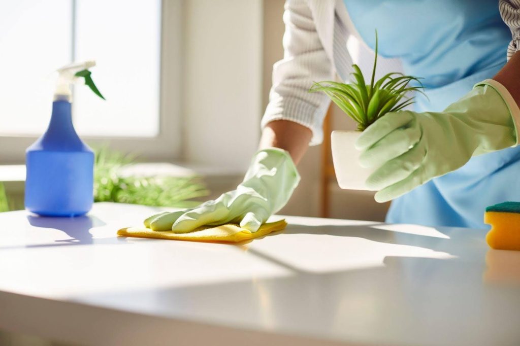 A woman in a blue apron is diligently cleaning a table with a cloth in a bright well-lit room