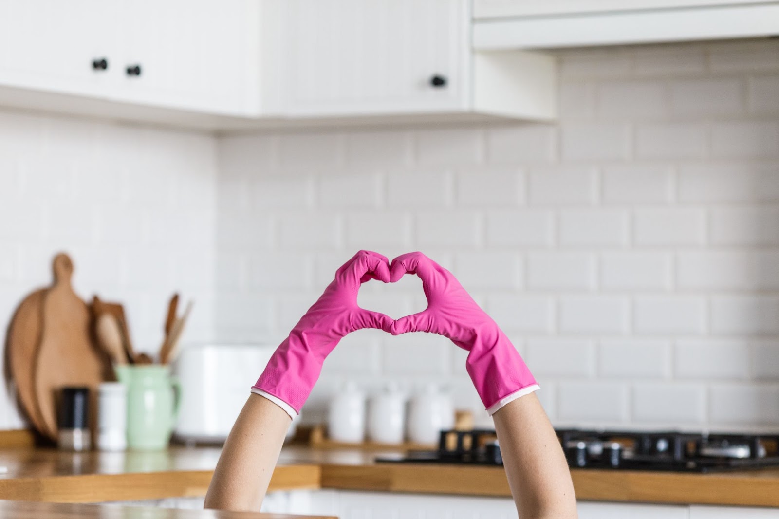 A person wearing pink gloves forms a heart shape with their hands in a modern kitchen.