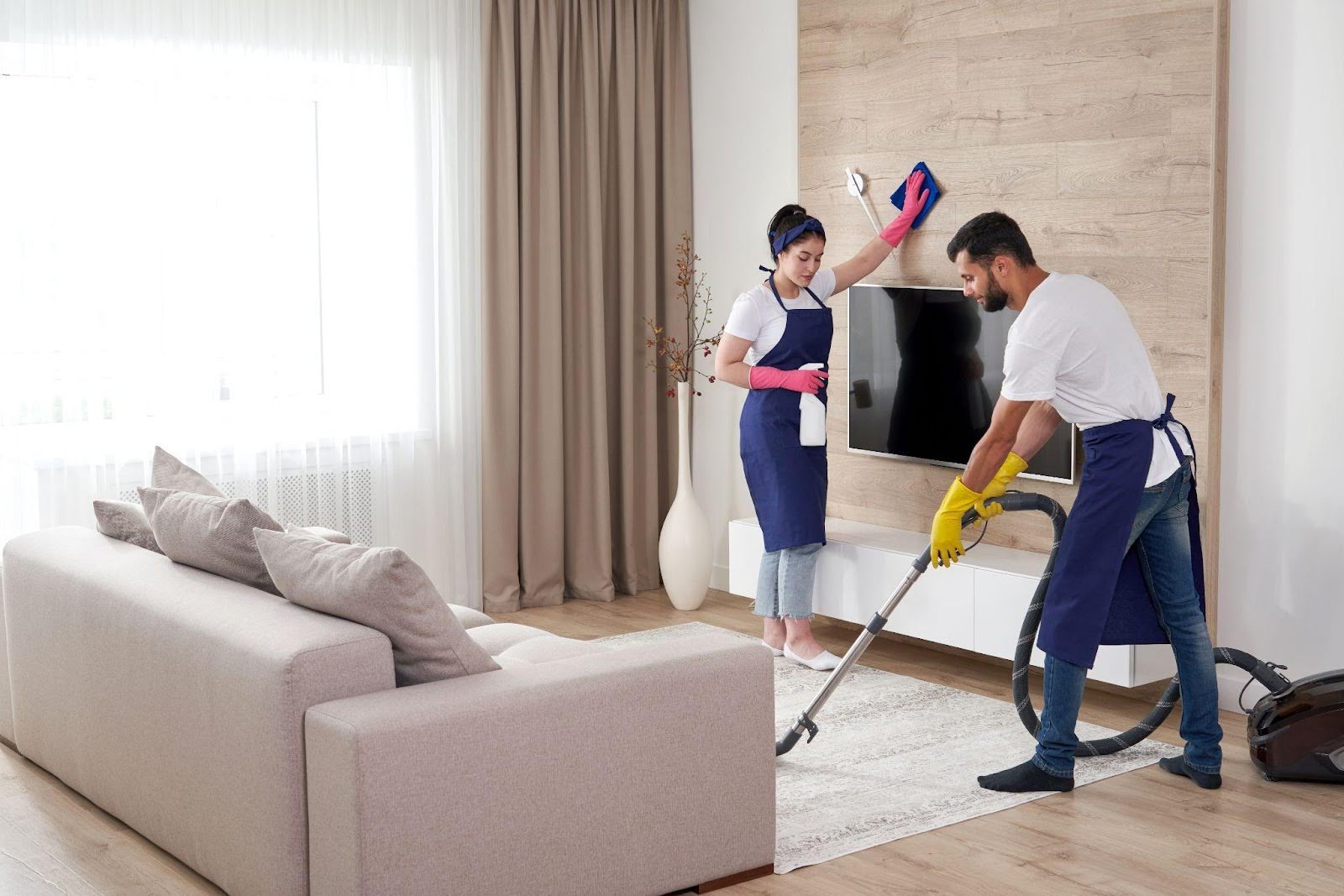 Two people cleaning a living room with a vacuum, showcasing teamwork
