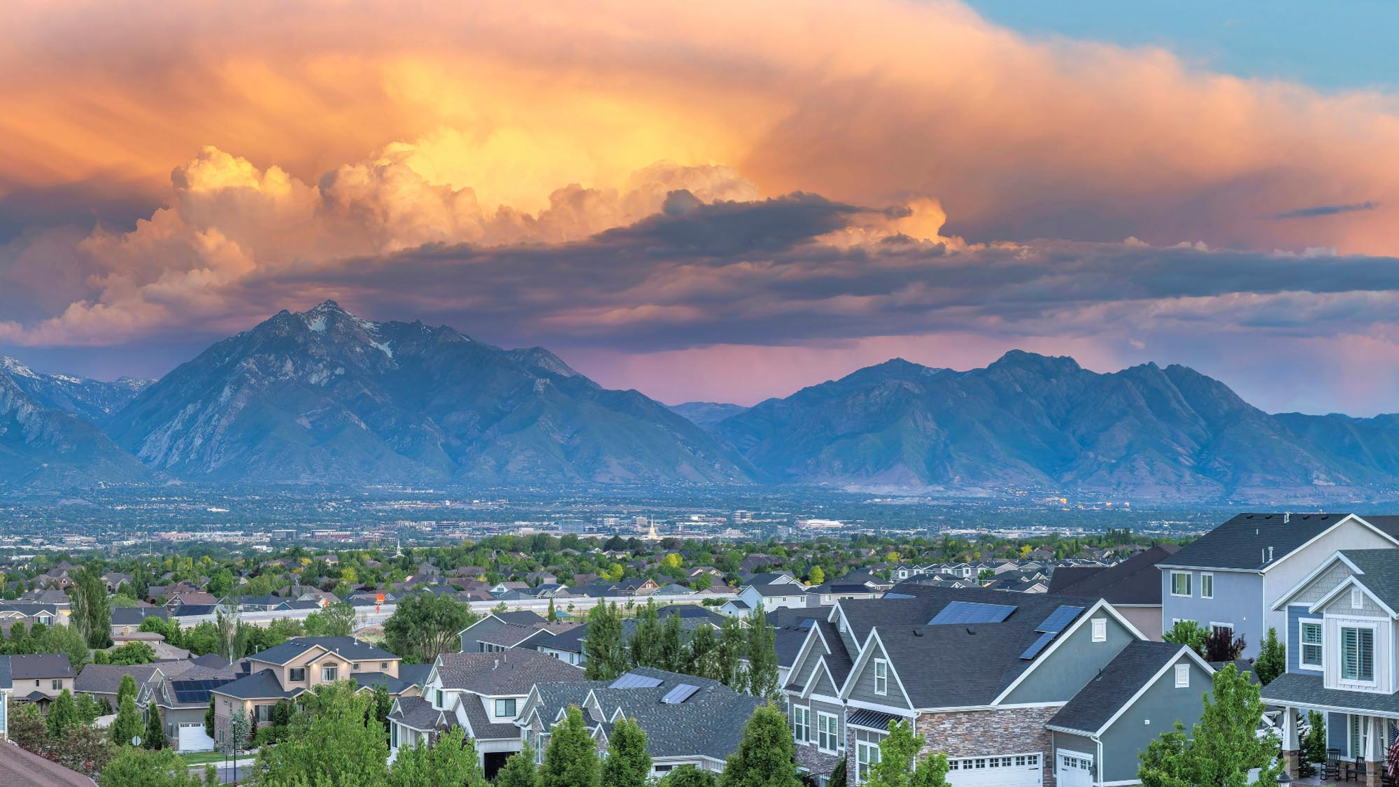 stunning sunset casts vibrant colors over a city, framed by majestic mountains in the background.