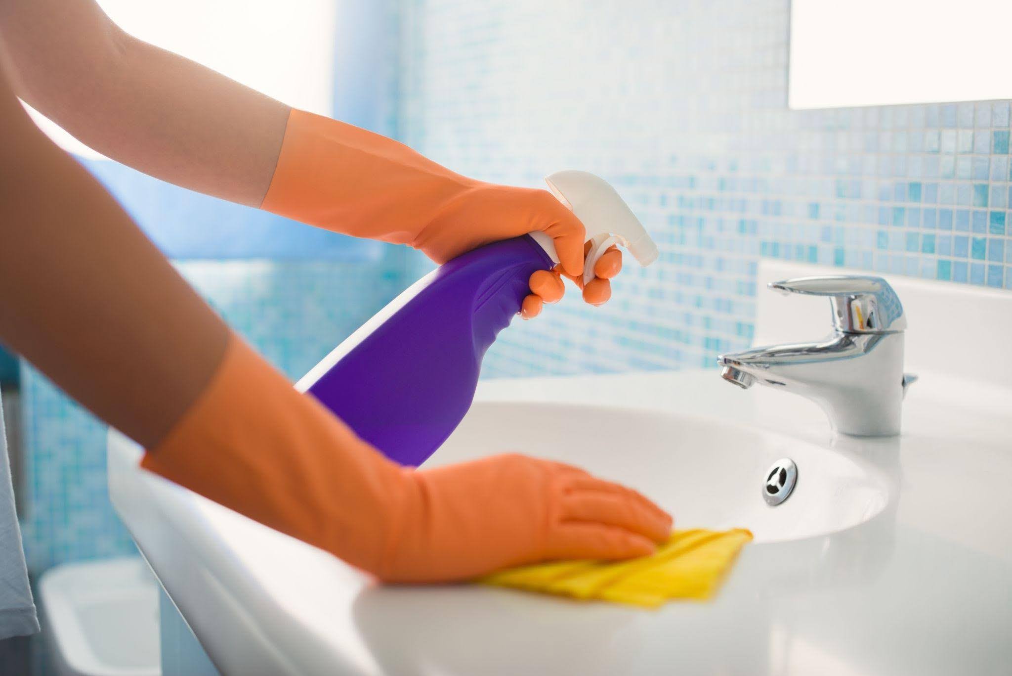 A person in rubber gloves cleans a bathroom sink ensuring hygiene
